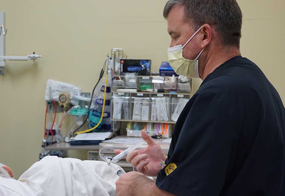 Healthcare professional wearing a mask and dark scrubs interacting with a patient in an outpatient setting.