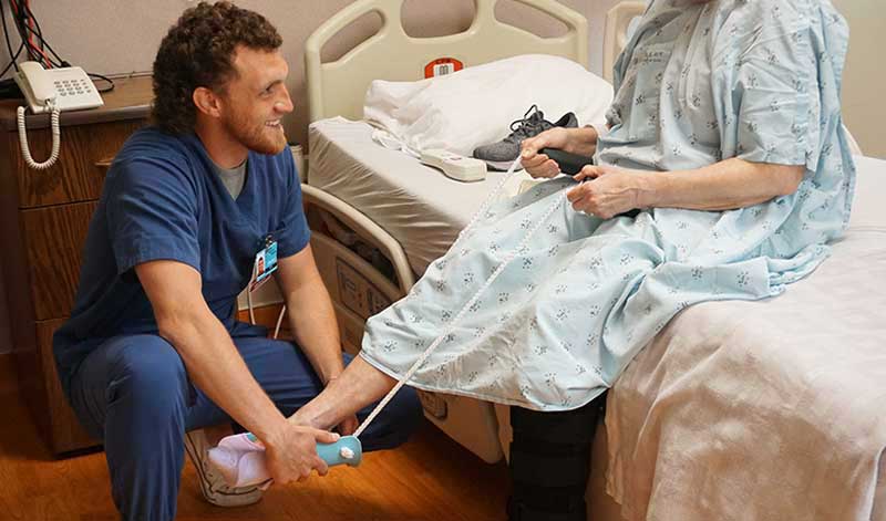 Pershing Health System occupational therapy team member assists a patient with a dressing activity while seated on a hospital bed.
