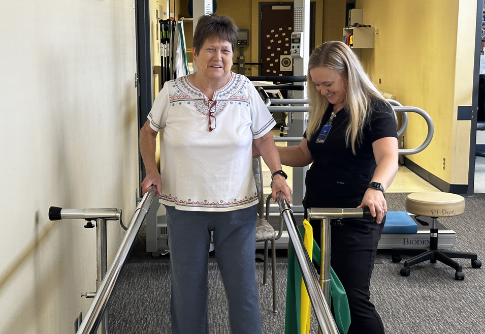 A physical therapy team member at Pershing Health System assists a patient with walking exercises using parallel bars in the rehabilitation department.