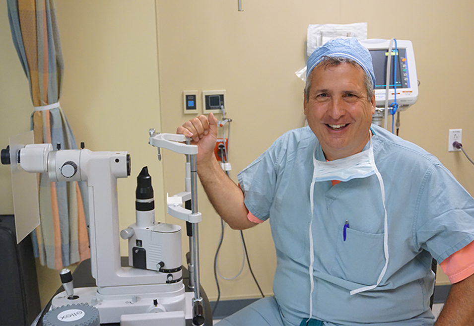 Dr. Andrew Moyes smiling next to eye examination equipment in a clinical setting.