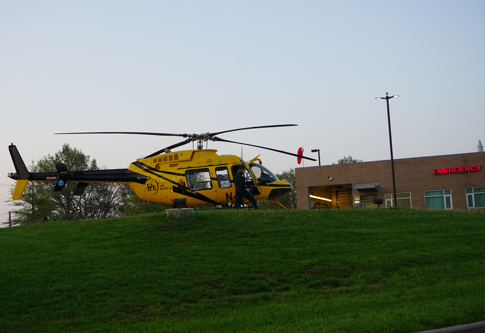Yellow and black LifeFlight helicopter parked on a grassy hill outside a brick medical building.